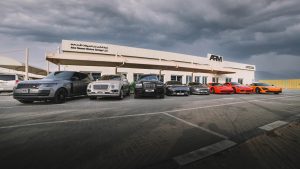 A large, brightly lit ARM MOTORS workshop in Dubai with several Porsches being serviced by staff