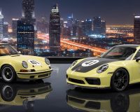 A vintage and a modern yellow Porsche, both featuring the racing number 41 and black decals, are parked in a rustic industrial garage